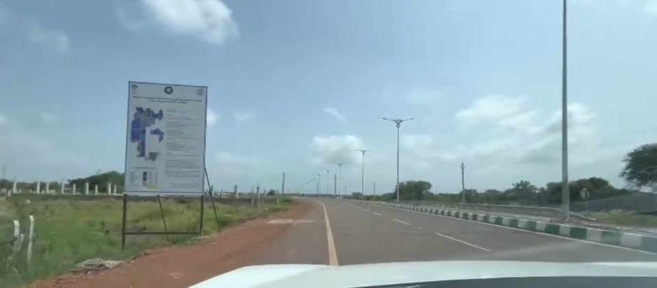 The NIMZ Phase-I project board beside a new, empty multi-lane road with street lights and a fence line, under a cloudy sky