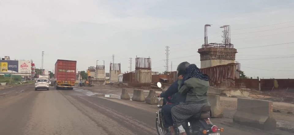 Elevated corridor piers under construction with exposed rebar beside a diverted traffic lane
